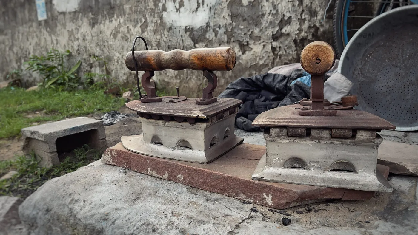 Two old charcoal box irons resting on a stone step outside a laundry